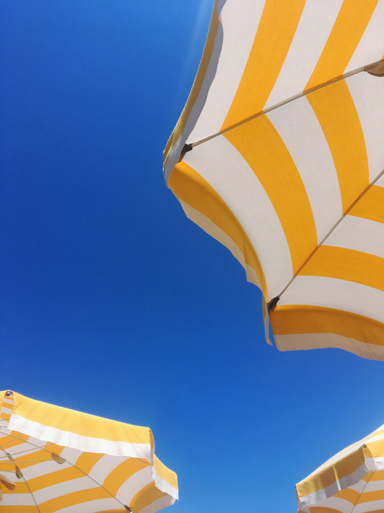 Bottom view of a yellow and white sunbrella on the beach or near a pool